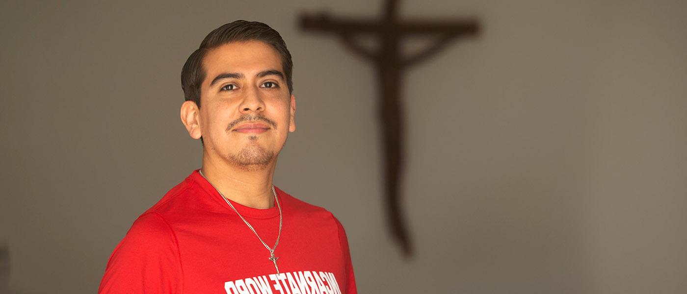 Pastoral Institute student in a chapel posing in front of a wall with a crucifix on it